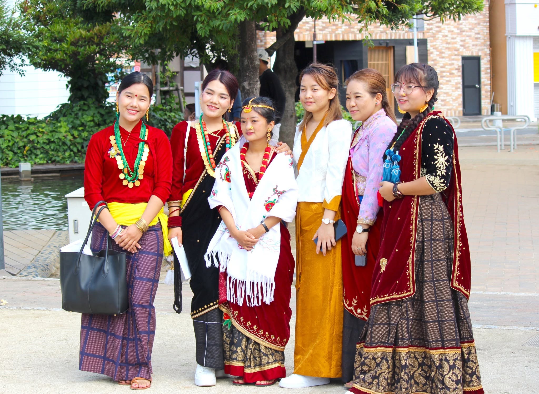 Six women in the traditional dress of different parts of Nepal, standing together by the water